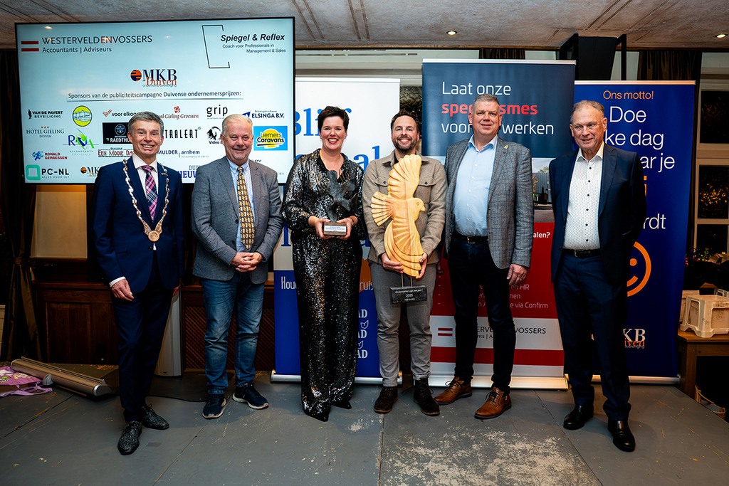 winnaars staan omringd door jury en burgemeester met hun prijzen in de hand.
