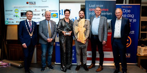 winnaars staan omringd door jury en burgemeester met hun prijzen in de hand.