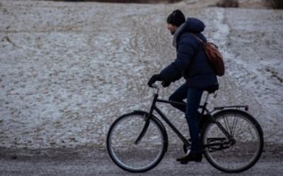 Jonge man met winterjas, sjaal en muts fietst over een onverharde weg